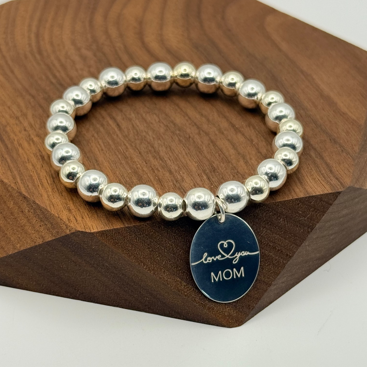 Silver beaded bracelet with a blue tag on a wooden surface