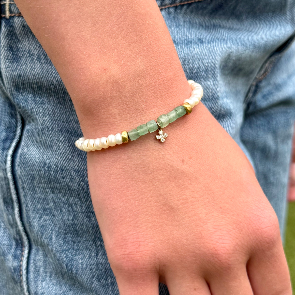 Close-up of a wrist wearing a bracelet with pearls and green beads, against a denim background.