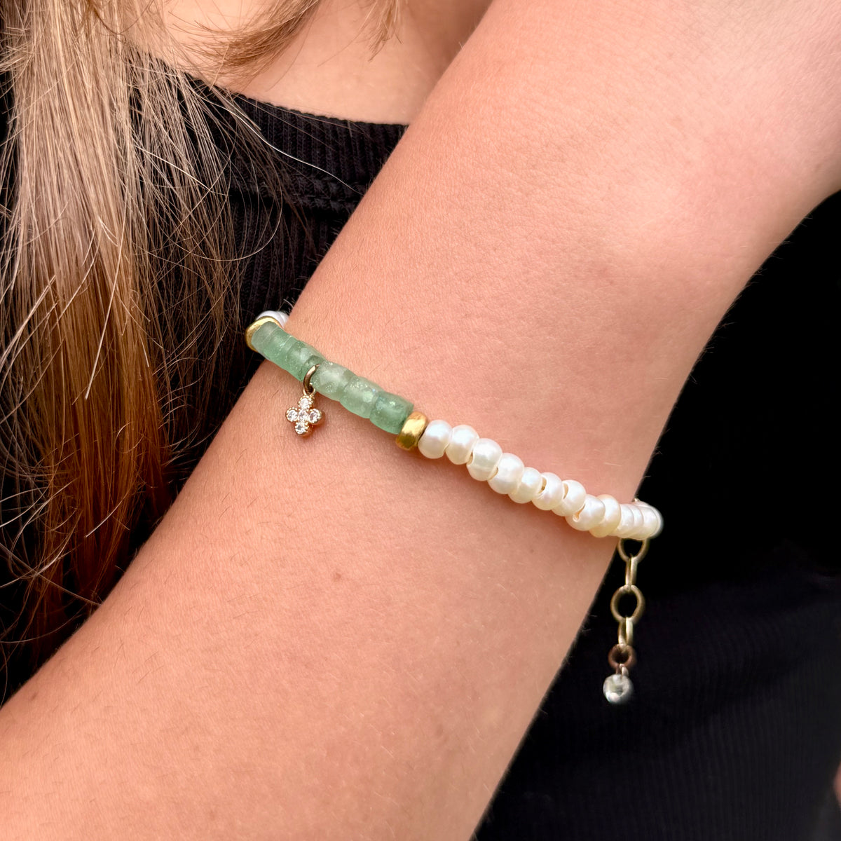 Bracelet with green beads and gold accents on a person's wrist against a black background