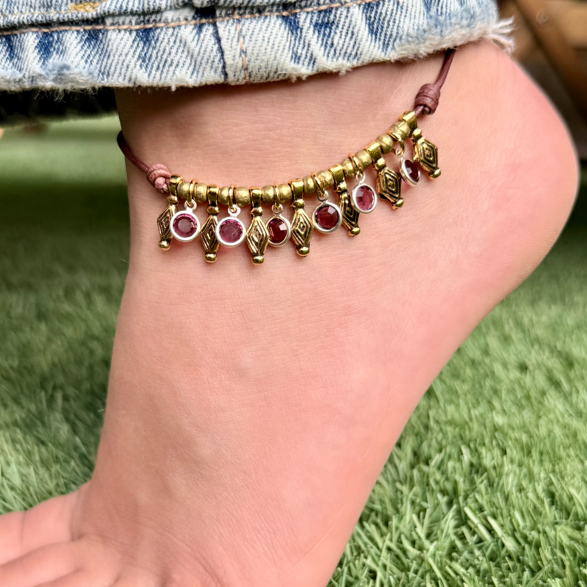 Ankle bracelet with gold and red beads on a foot against a grass background