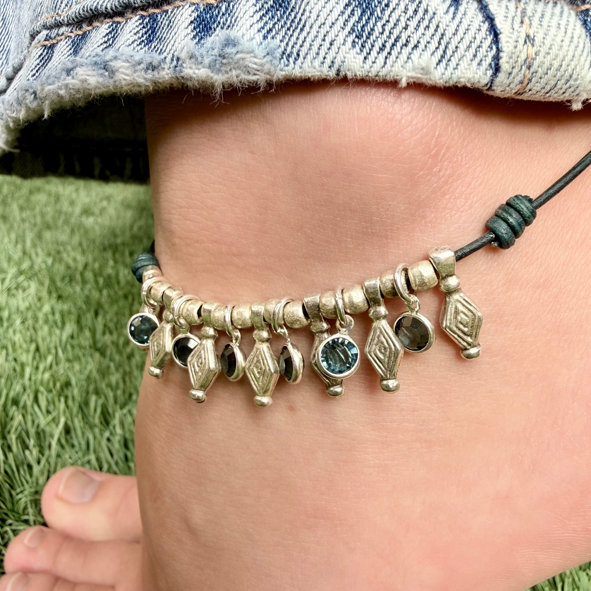 Close-up of a anklet with beads on a person's ankle against a grass background