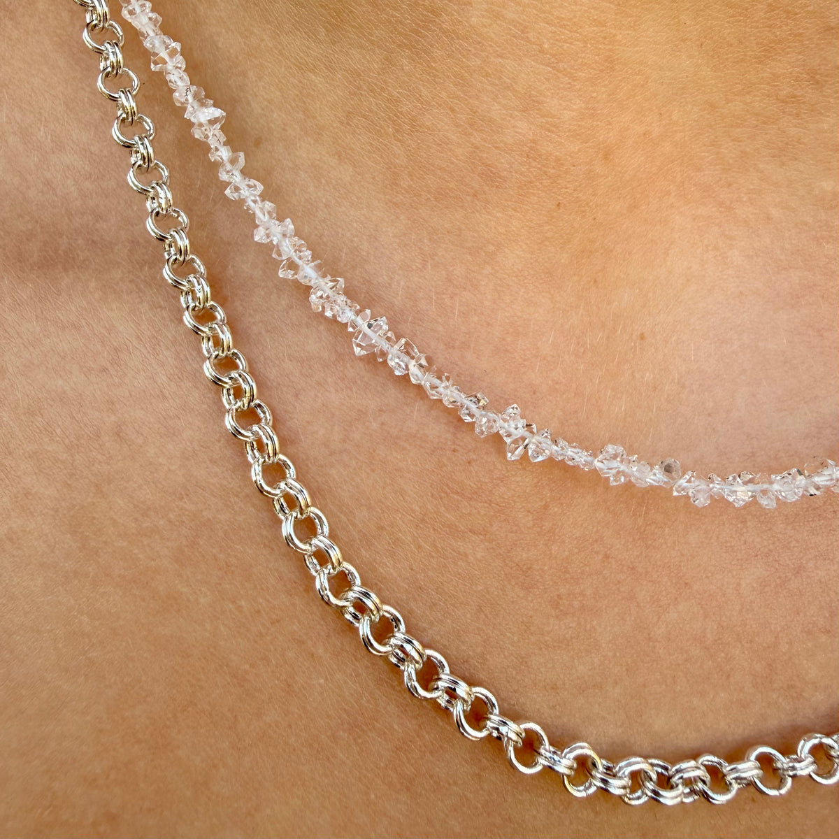 Two silver necklaces on a person's neck with a blurred background