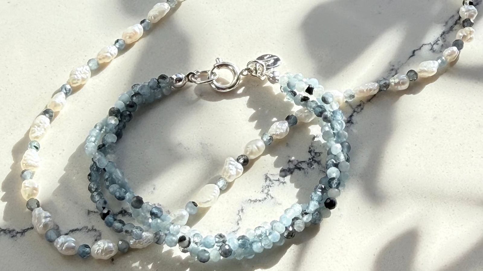 Photo of the an aquamarine bracelet and necklace laying flat on a white stone countertop.