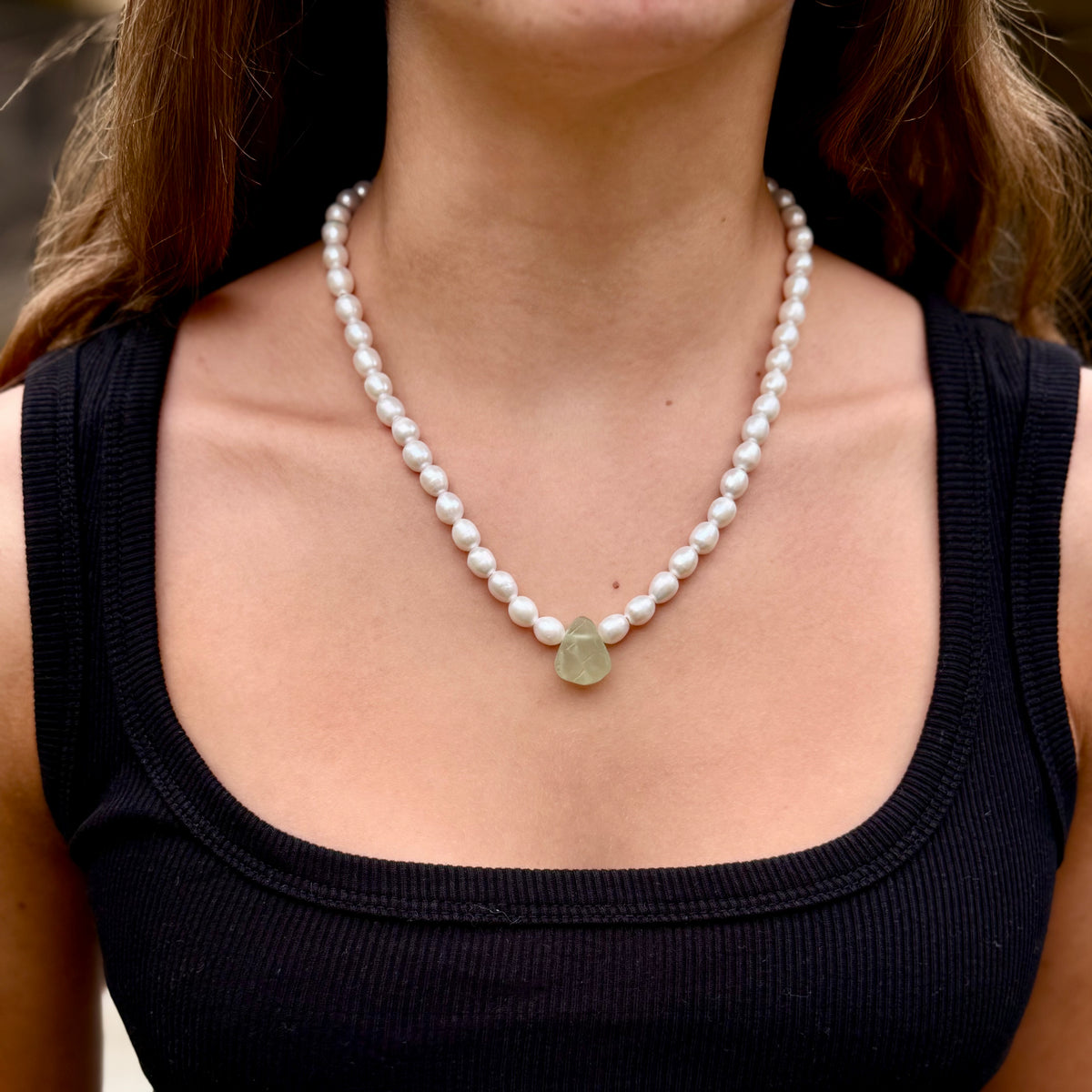 Pearl necklace with a pendant worn by a person in a black top.