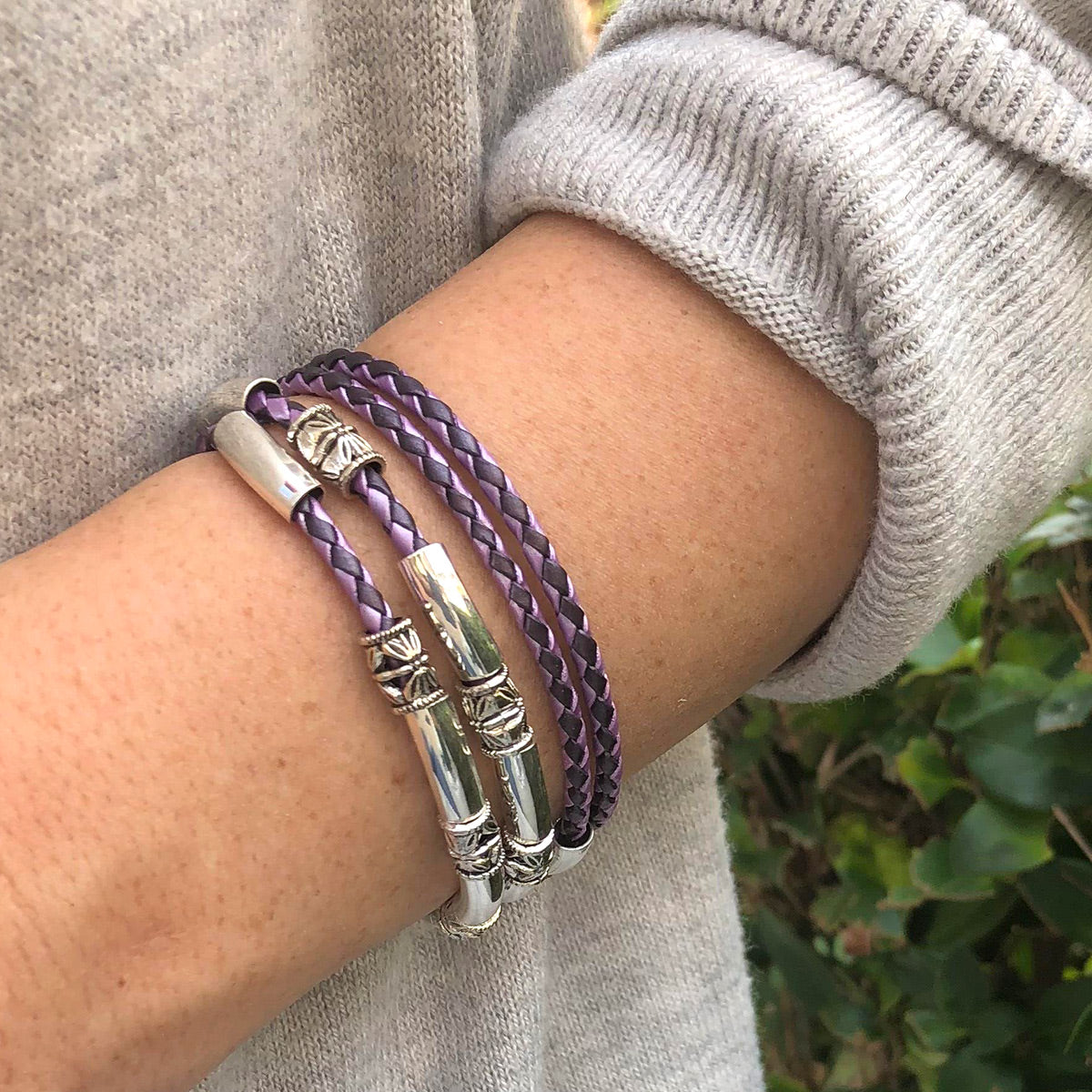 Purple braided bracelet with silver accents on a wrist, wearing a gray sweater.