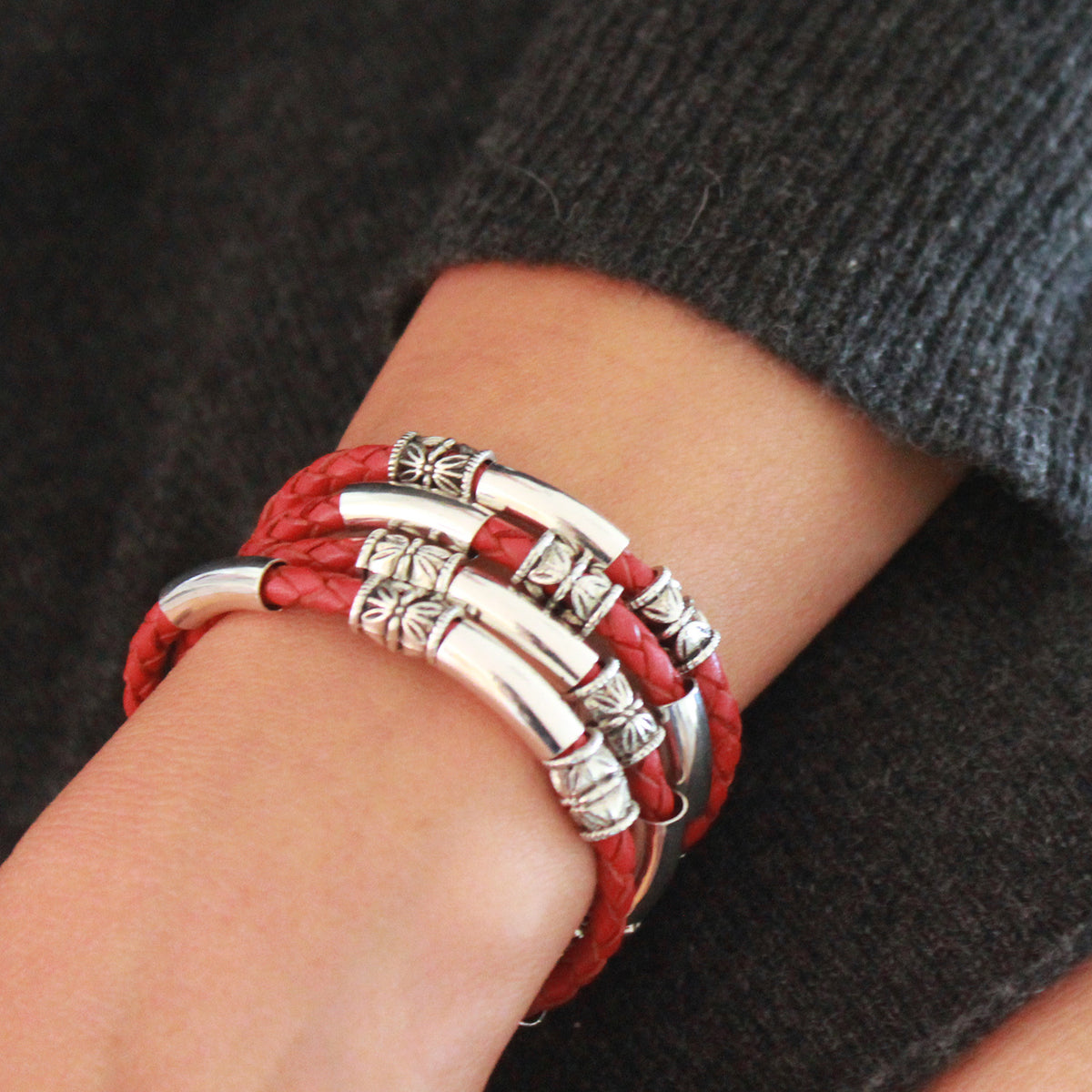 Red leather bracelet with silver beads on a wrist against a dark background