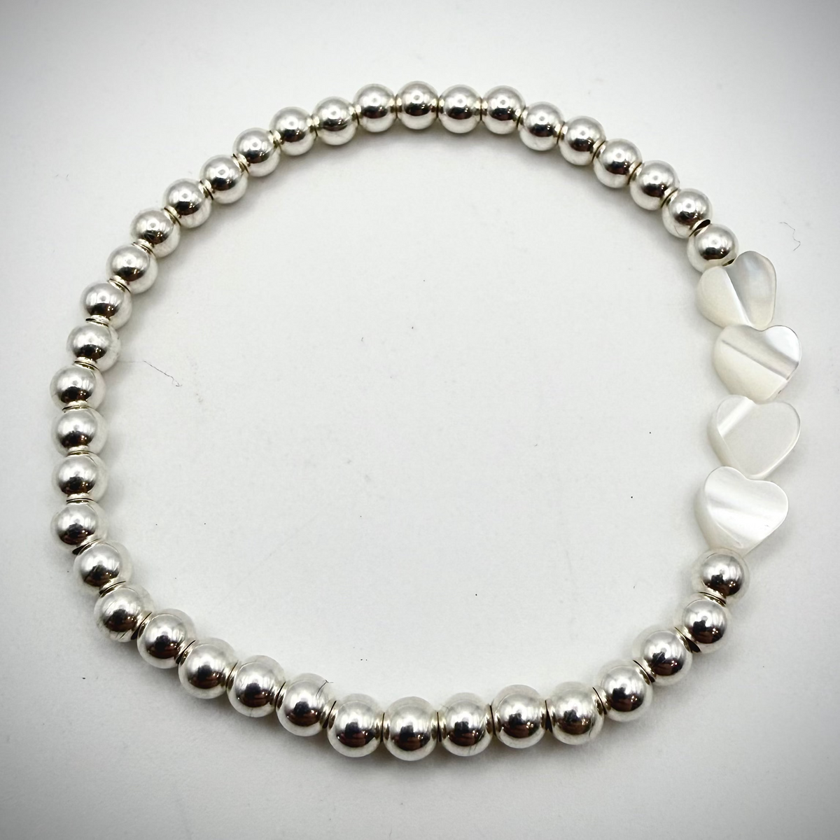 Dainty waterproof sterling silver bead stretch bracelet with four iridescent white Pearl mini heart beads.