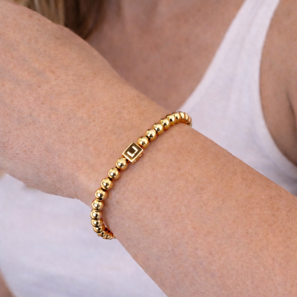 Gold beaded bracelet on a person's wrist with a white tank top