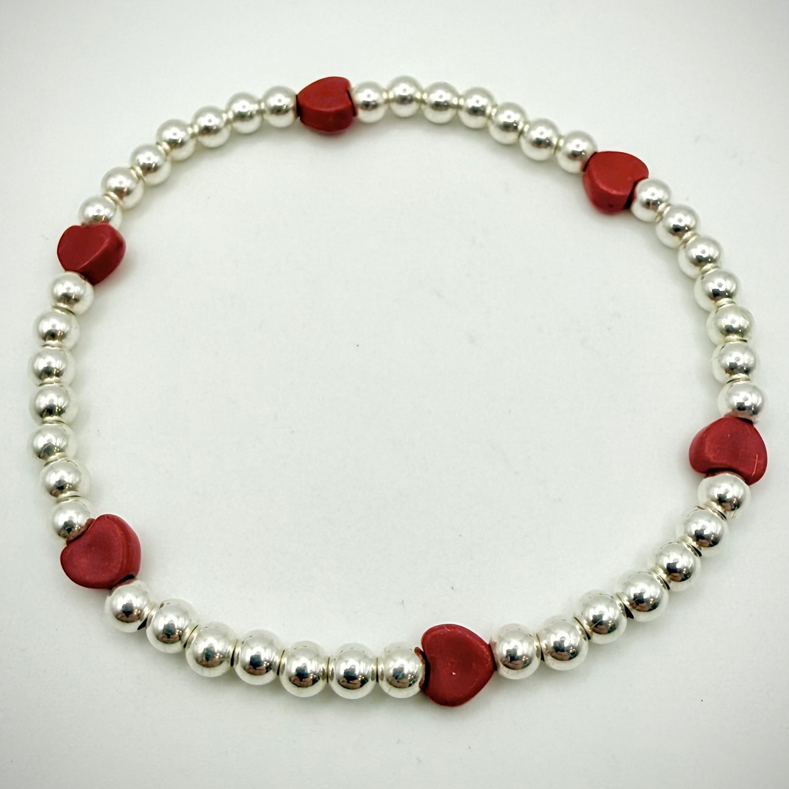 Bracelet with alternating red heart-shaped beads and silver beads on a white background