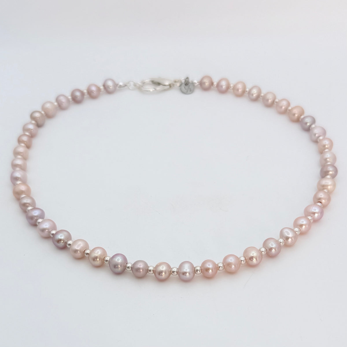 Studio flat lay photo of a Pink freshwater pearl necklace with naturally varied blush and mauve tones and small silver plated spacer beads on a white background. 