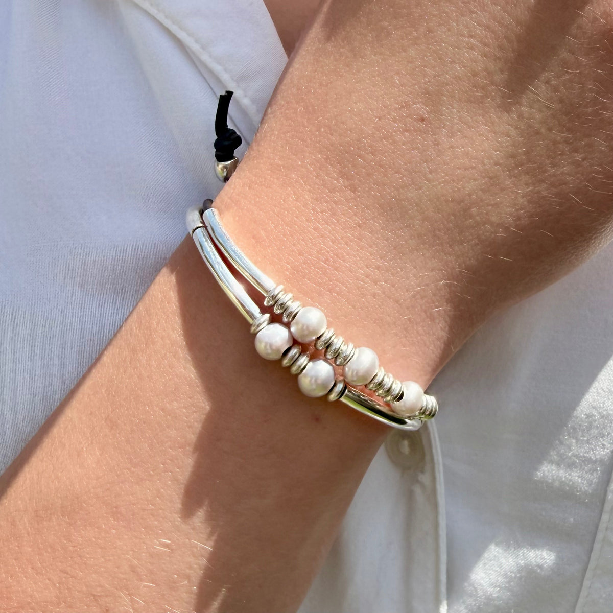 Close-up of a wrist wearing a silver and white beaded bracelet against a light background.