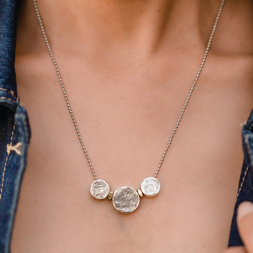 Necklace with three round pendants on a person wearing a blue denim jacket.