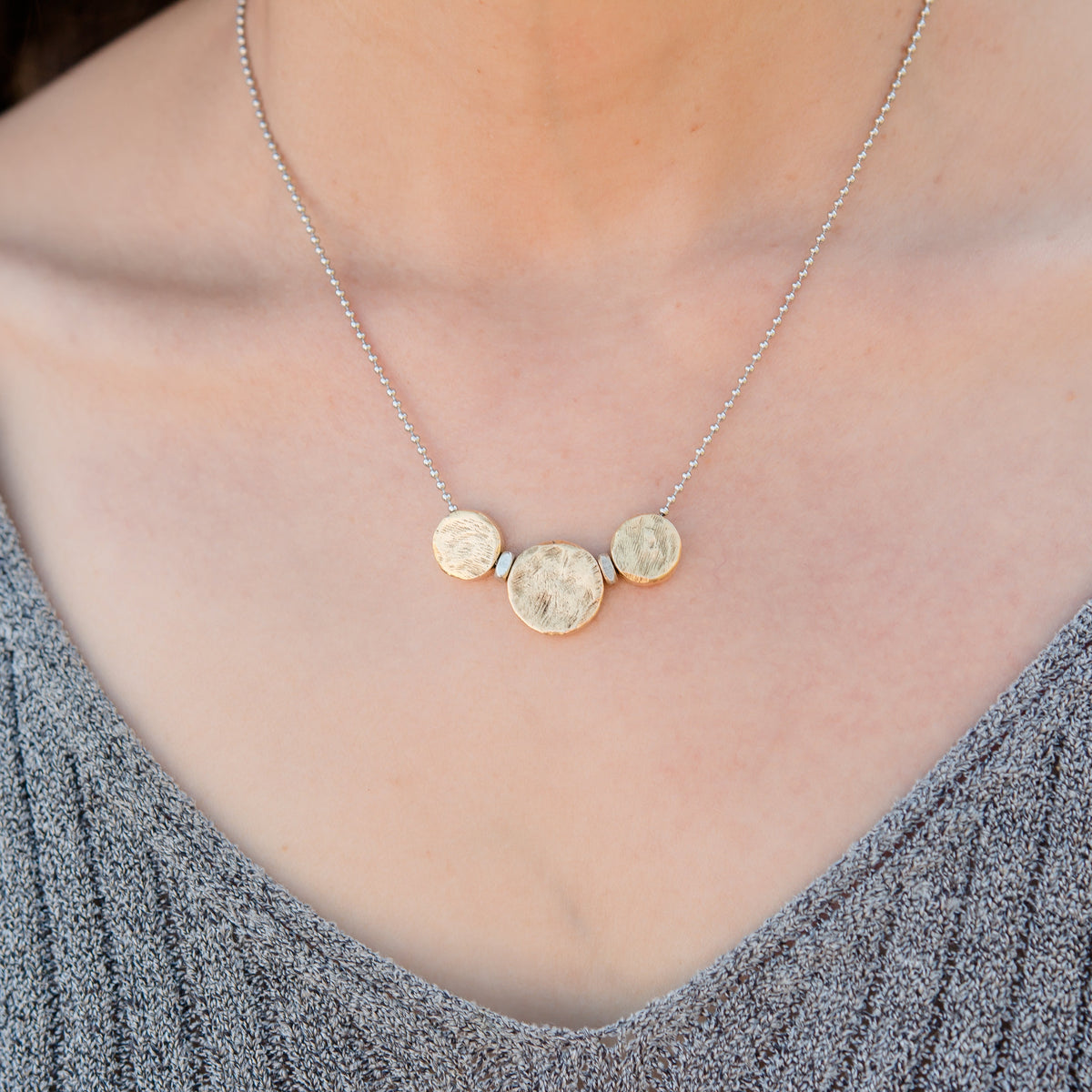 Necklace with circular pendants on a person wearing a gray sweater