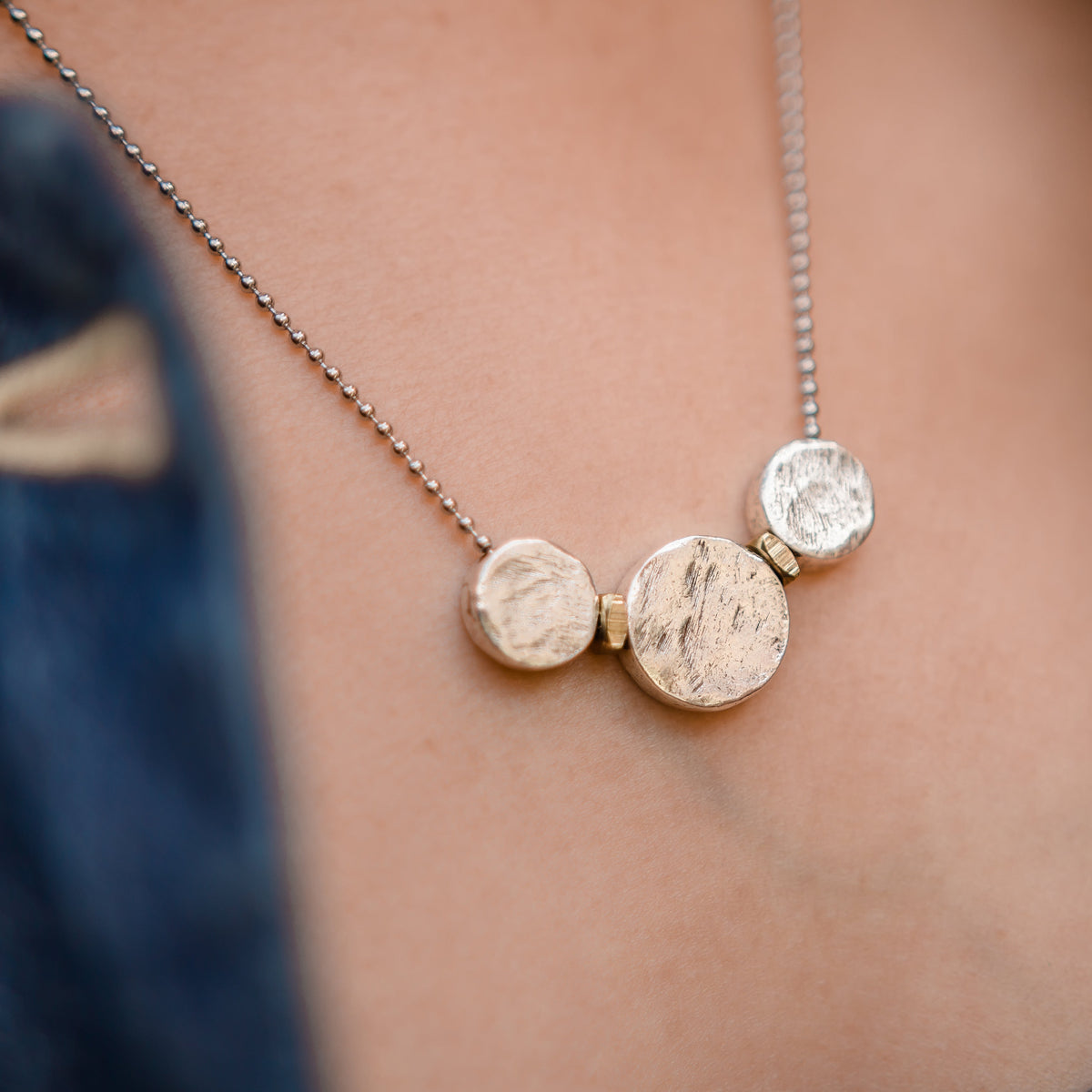 Necklace with three round pendants on a person wearing a denim jacket.