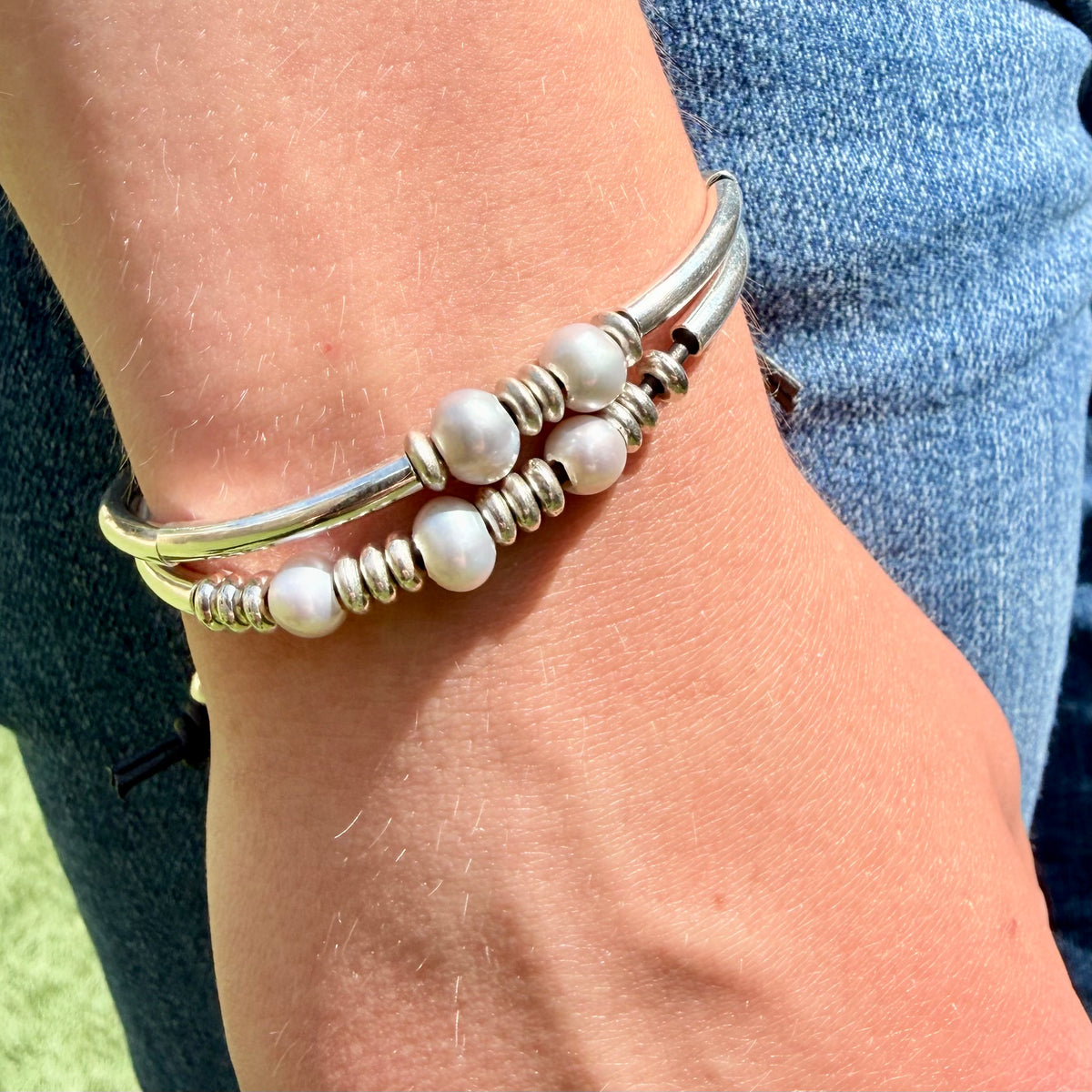 Silver bracelet with pearl-like beads on a wrist against a blue denim background