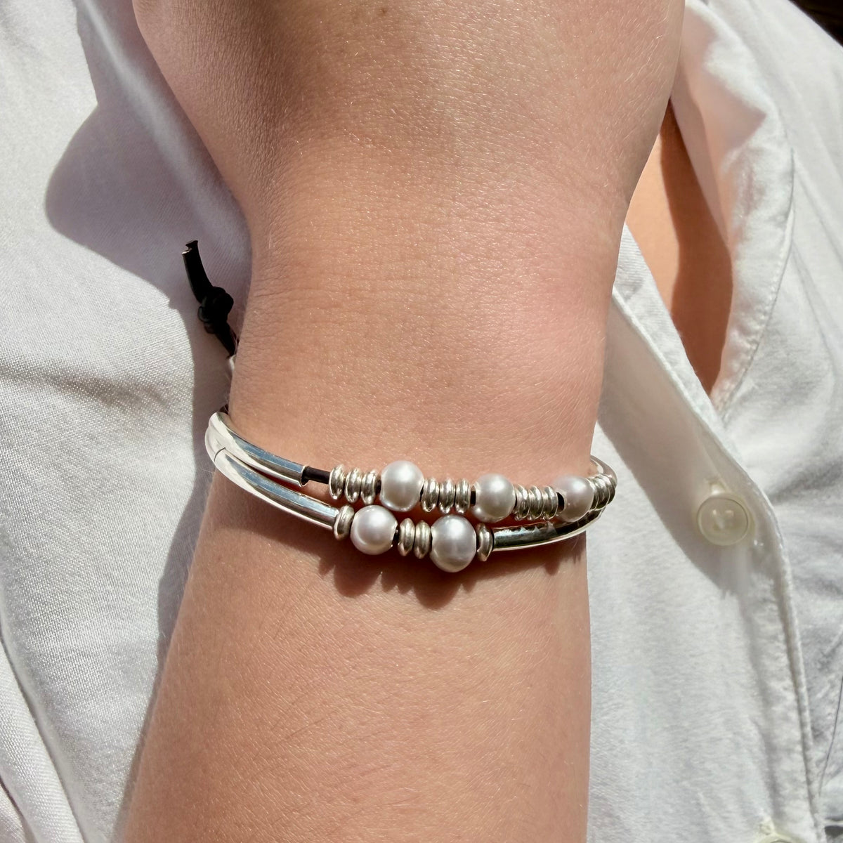 Close-up of a wrist wearing a silver bracelet with pearl-like beads against a light background.