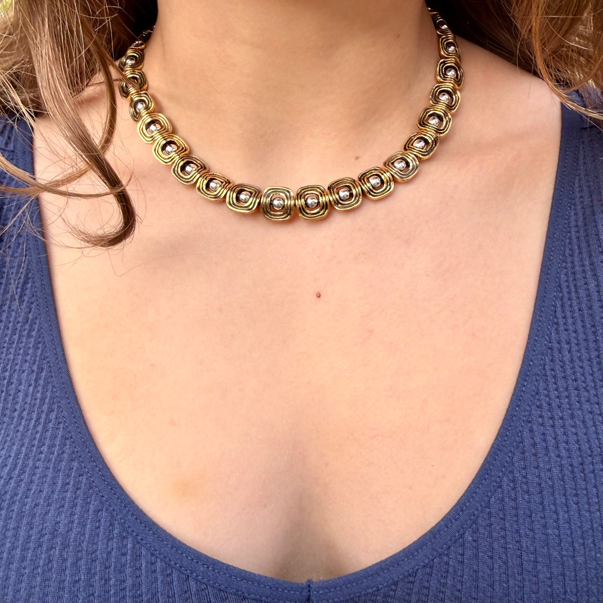 Close-up of a person wearing a gold necklace with a blue top.