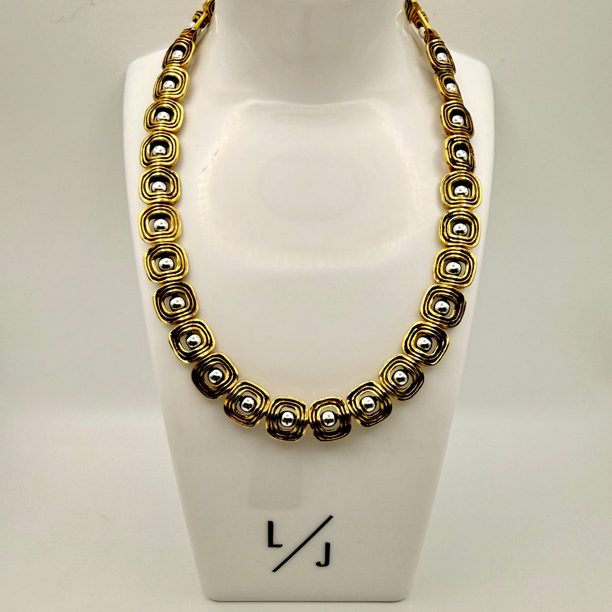 Gold and silver necklace on a mannequin bust with 'LJ' branding.