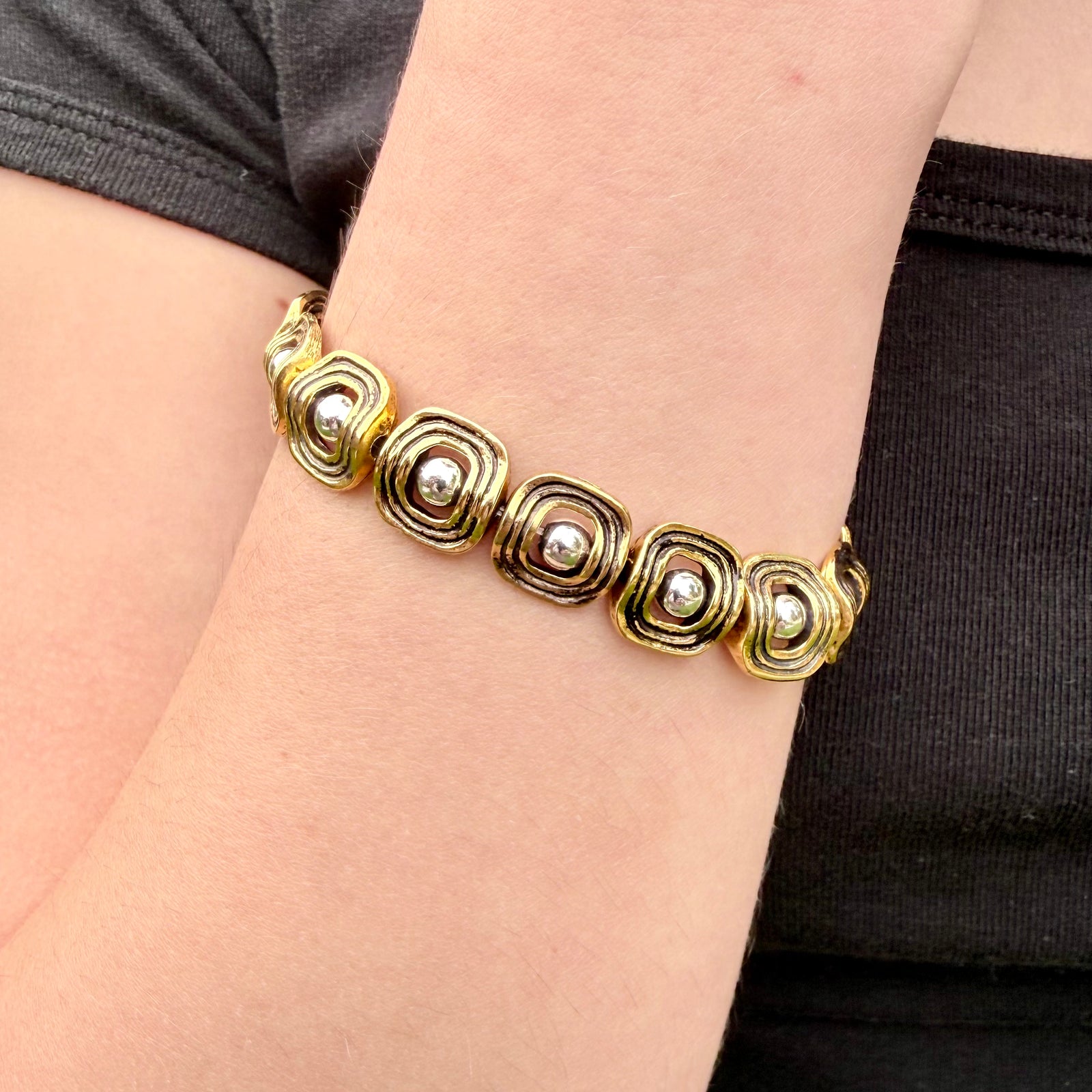 Gold bracelet with circular designs on a wrist against a black background