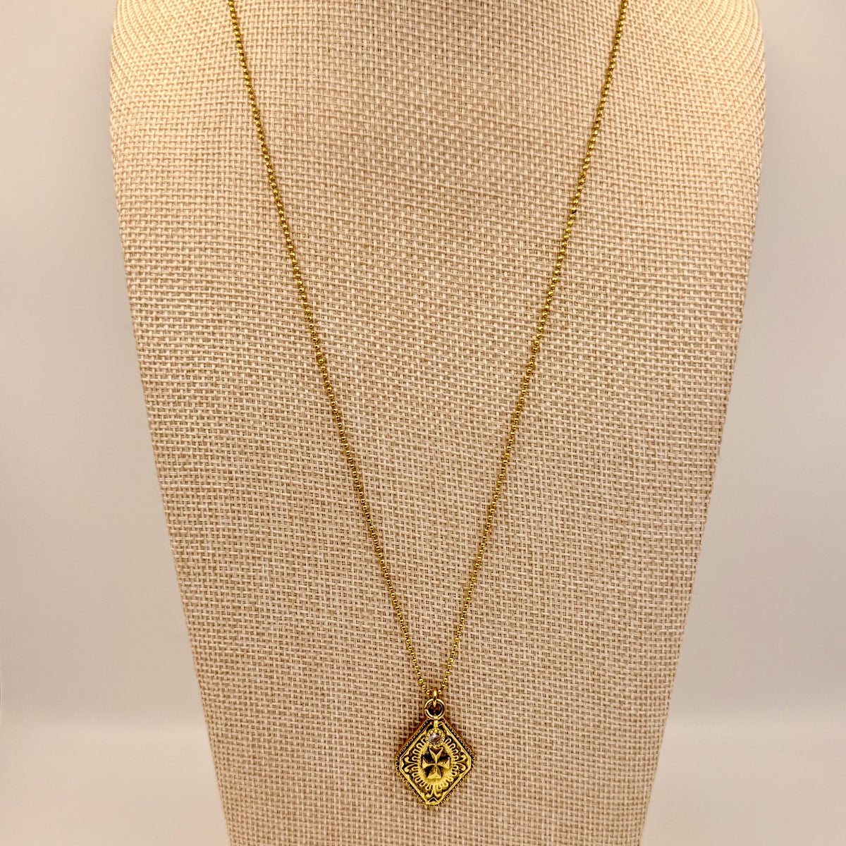 Gold necklace with a pendant on a beige mannequin bust.