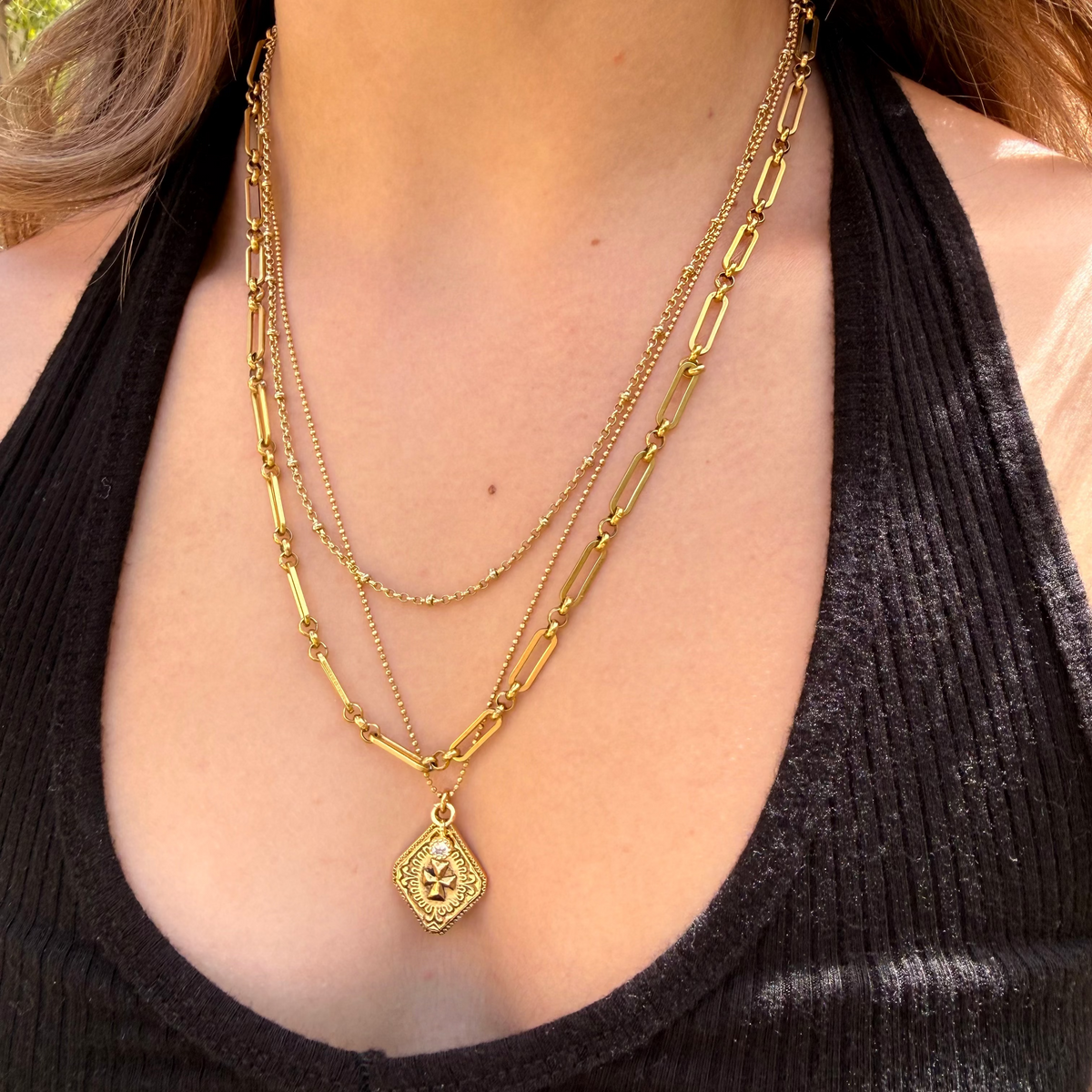 Close-up of a person wearing multiple gold necklaces with a black top.