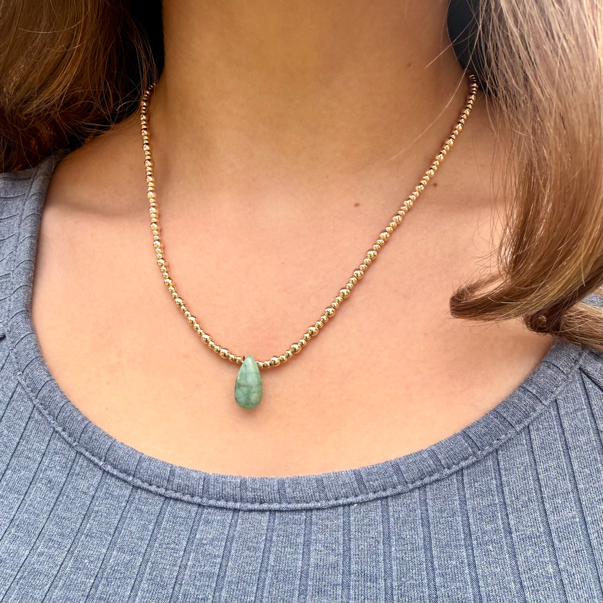 Necklace with a green pendant worn by a person in a blue top