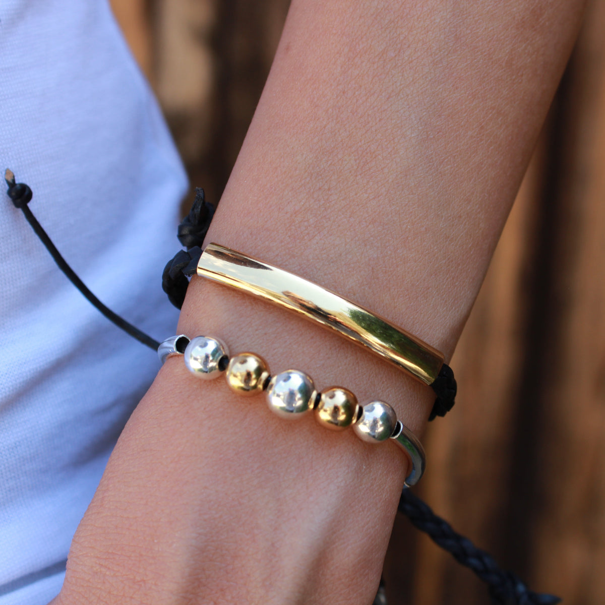 Close-up of a wrist wearing a gold bracelet with silver beads against a blurred background