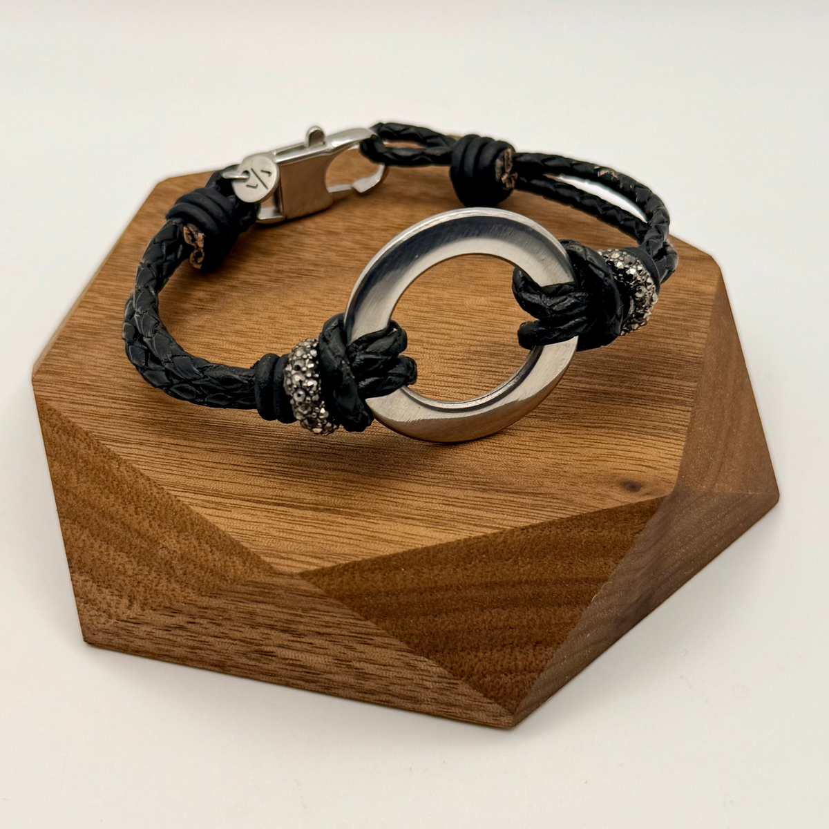 Bracelet with black cord and silver circular clasp on a wooden stand