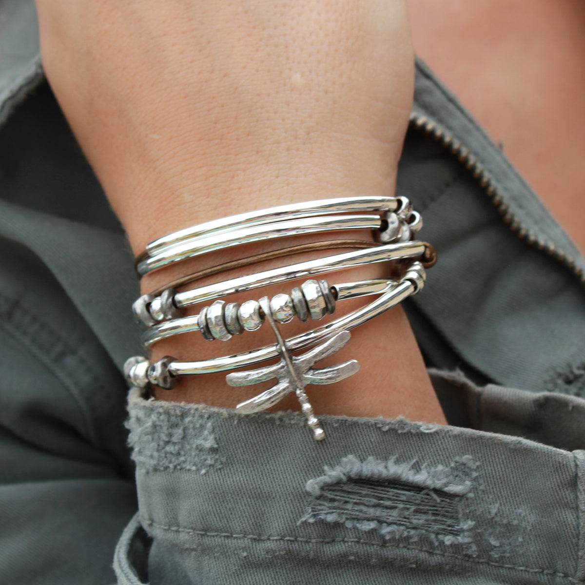 Silver bracelet with dragonfly design on a wrist, wearing a gray jacket.