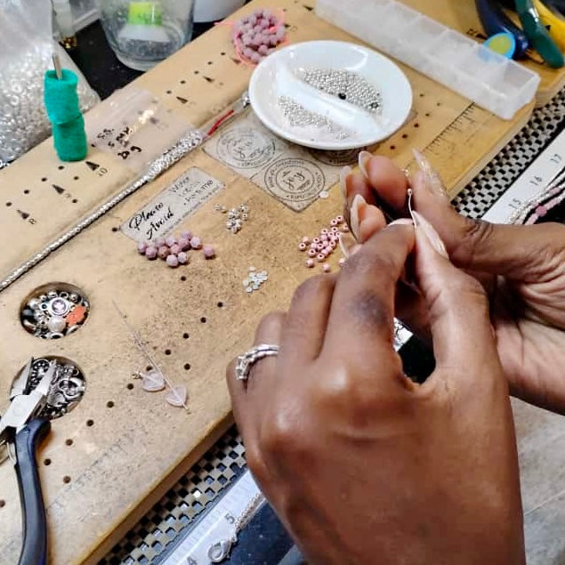 Close-up of hands working on jewelry with tools and materials on a table.
