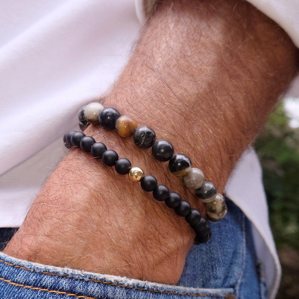 Men&#39;s black onyx beaded bracelet with 14k gold bead next to grey gemstone bead bracelet