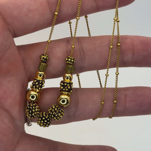 Gold necklace with assortment of gold beaded accent help in a hand showing the detail.
