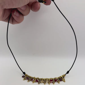 Video of Naya warm crystal necklace with garnet, ruby, and citrine dangles on black leather with antique gold details moving in the light