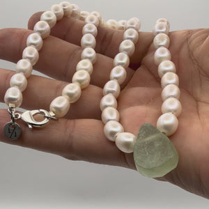 Hand holding pearl necklace with green glass stone bead pendant