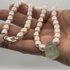 Hand holding pearl necklace with green glass stone bead pendant