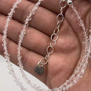 Close-up of a hand holding a clear crystal necklace held up close 
