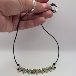 Video of hand holding a leather necklace with emerald, turquiose and peridot colored crystals and vintage silver colored beads