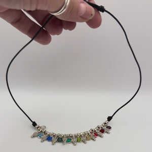 Video of a hand holding and showing the detail of a necklace with vintage silver tone beads and multi colored crystal dangles strung on black leather.